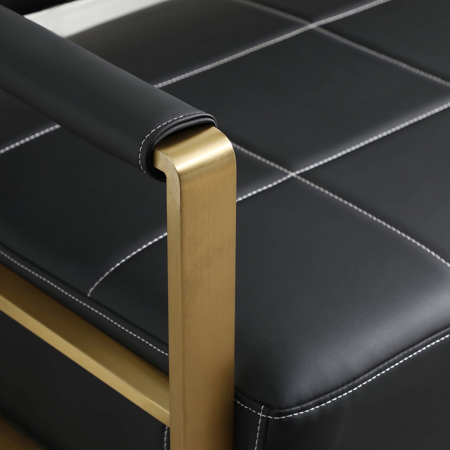 Black faux leather armchair with white stitching and gold metal legs