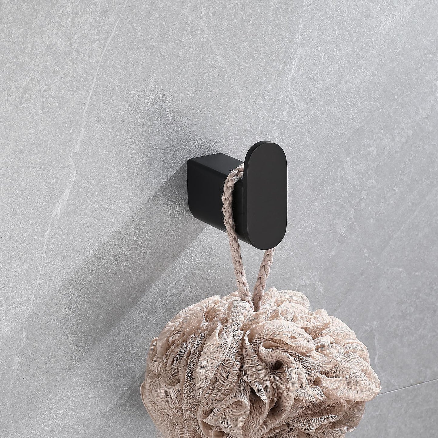 Black oval bathroom hook holding a beige loofah against a tiled wall