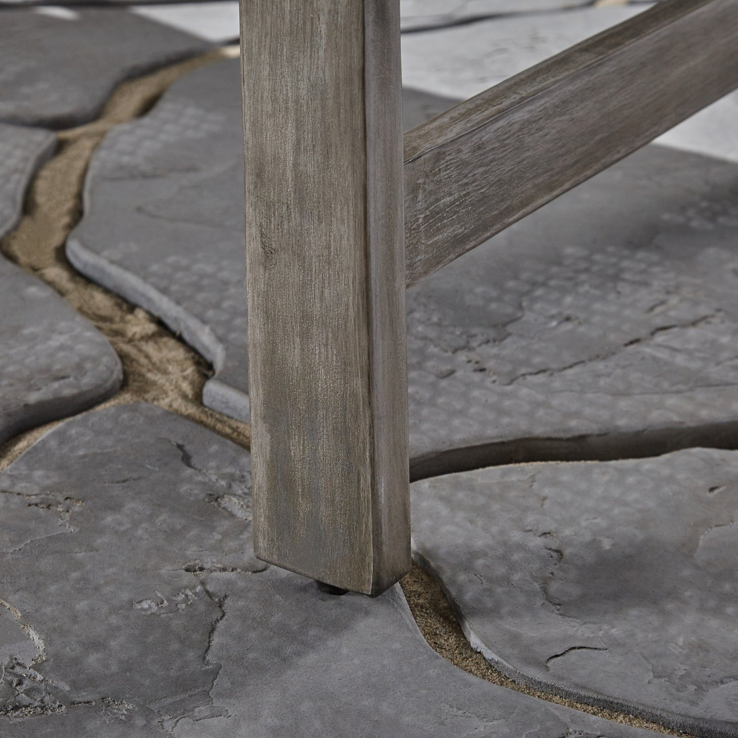 Weathered grey wood leg of a patio chair on a stone patio with sand filling