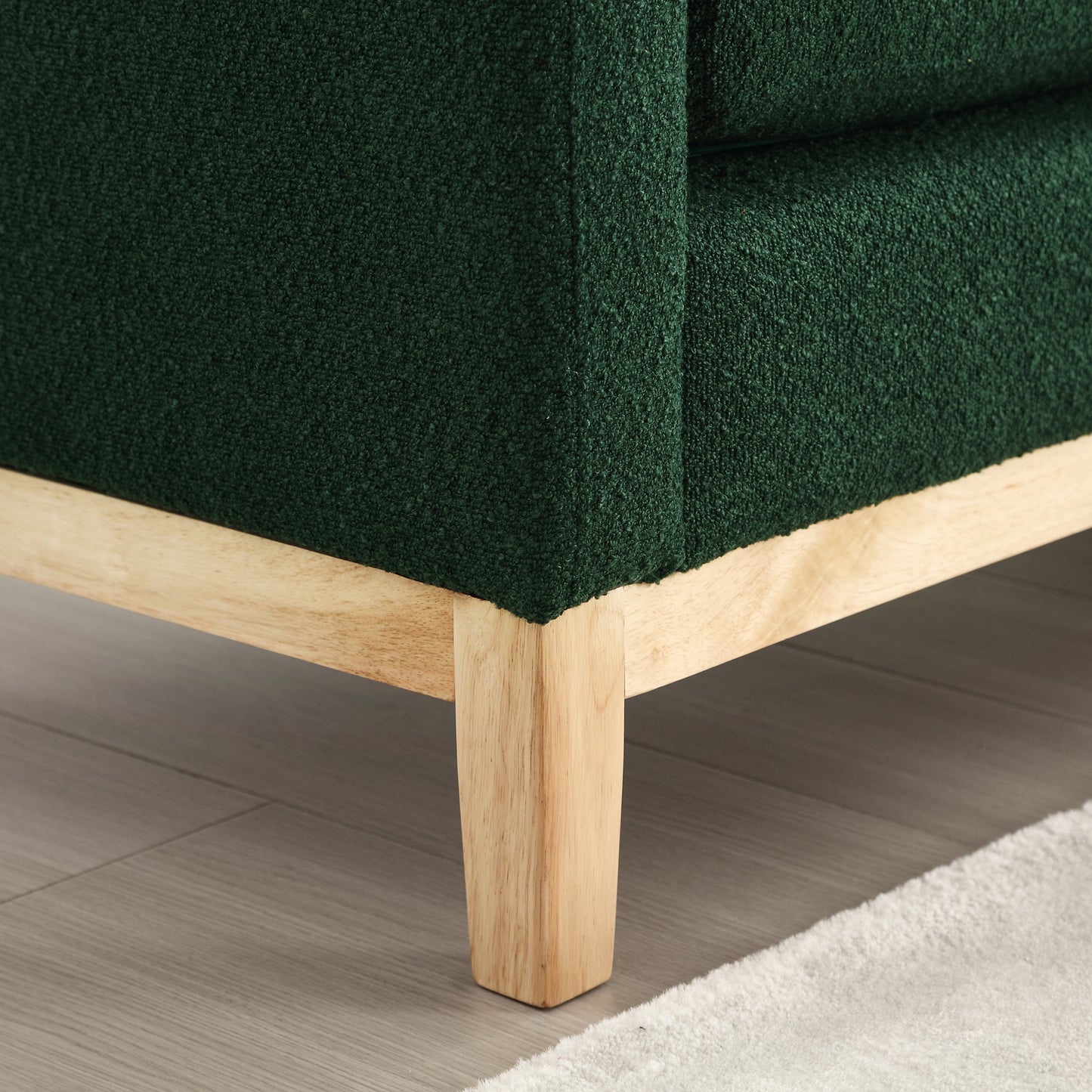 Closeup of deep emerald green boucle fabric sofa corner with natural wood legs