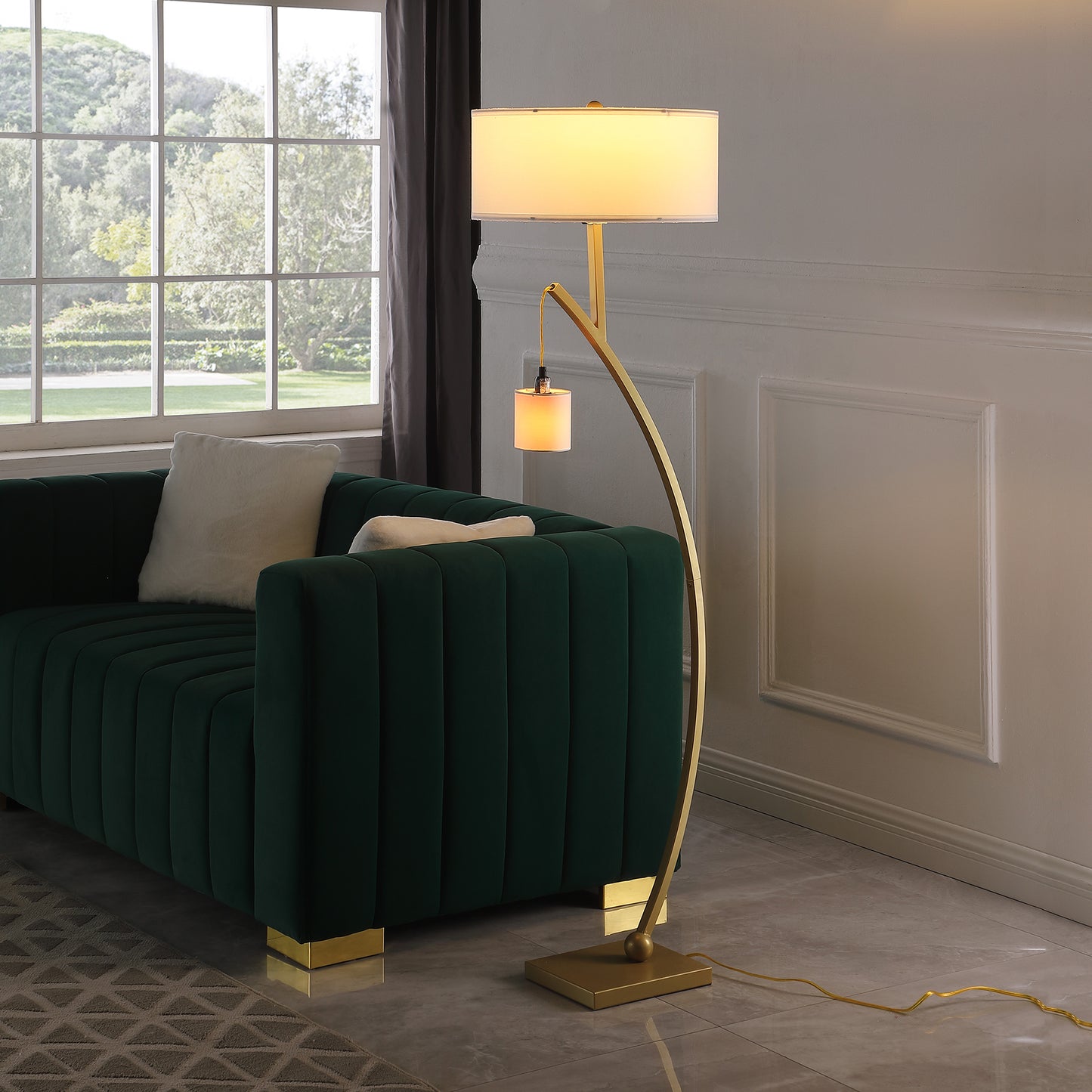 Elegant gold arc floor lamp with dual shades illuminating a plush green sofa