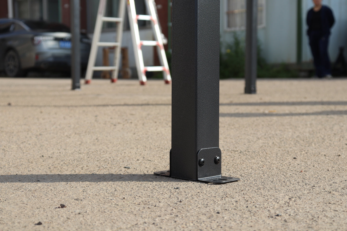 Black textured metal gazebo post with angled metal foot and two screws securing to ground