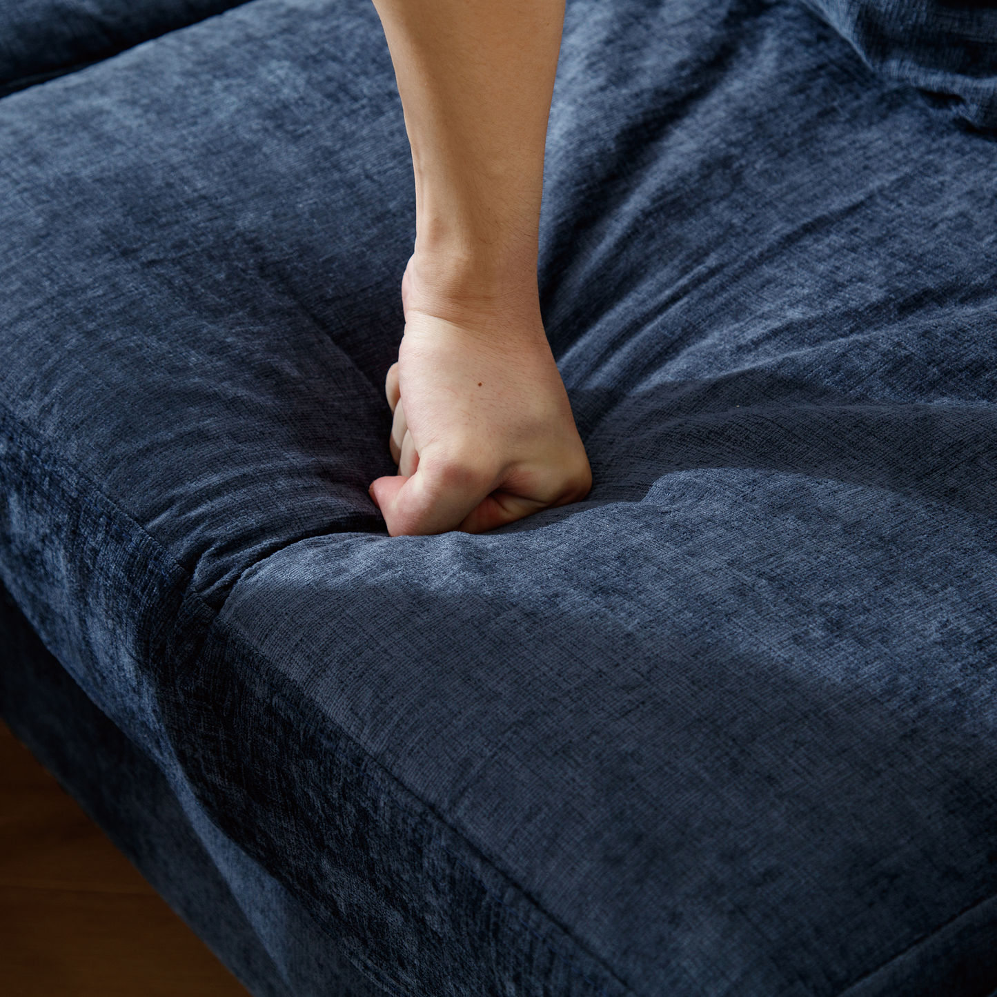 Closeup of a hand pressing into a plush navy blue fabric sofa cushion showcasing its deep comfort