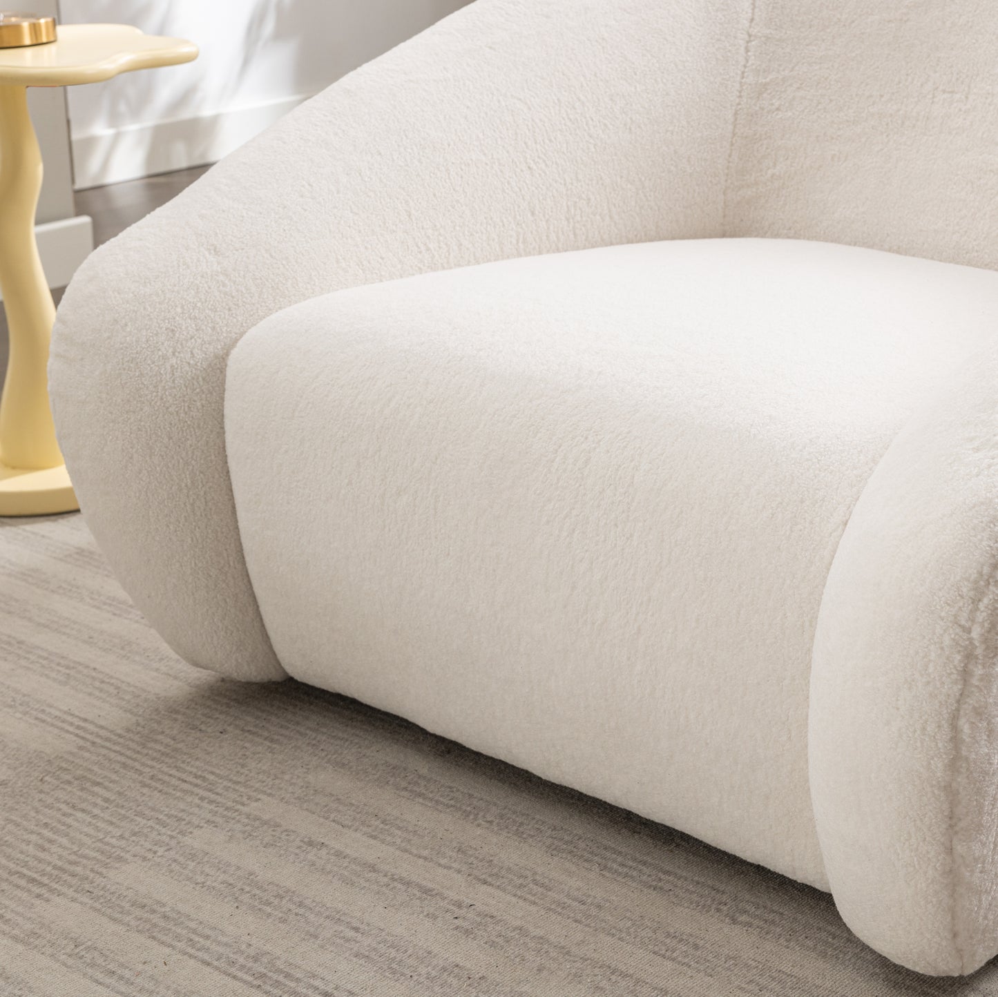 Cream boucl armchair with plush fabric texture and rounded armrest on a striped rug