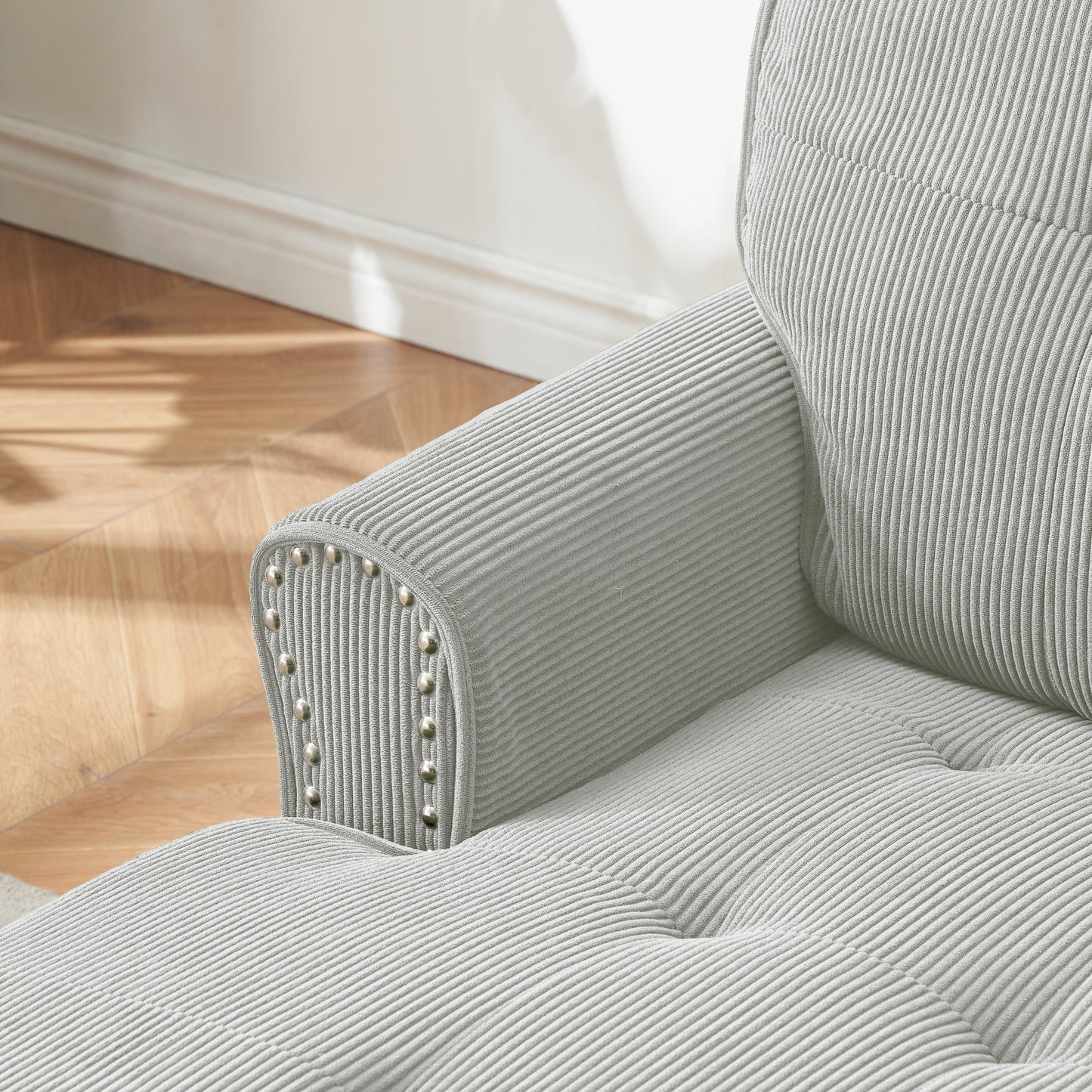Light gray corduroy sofa armrest with tufted buttons and nailhead trim accents