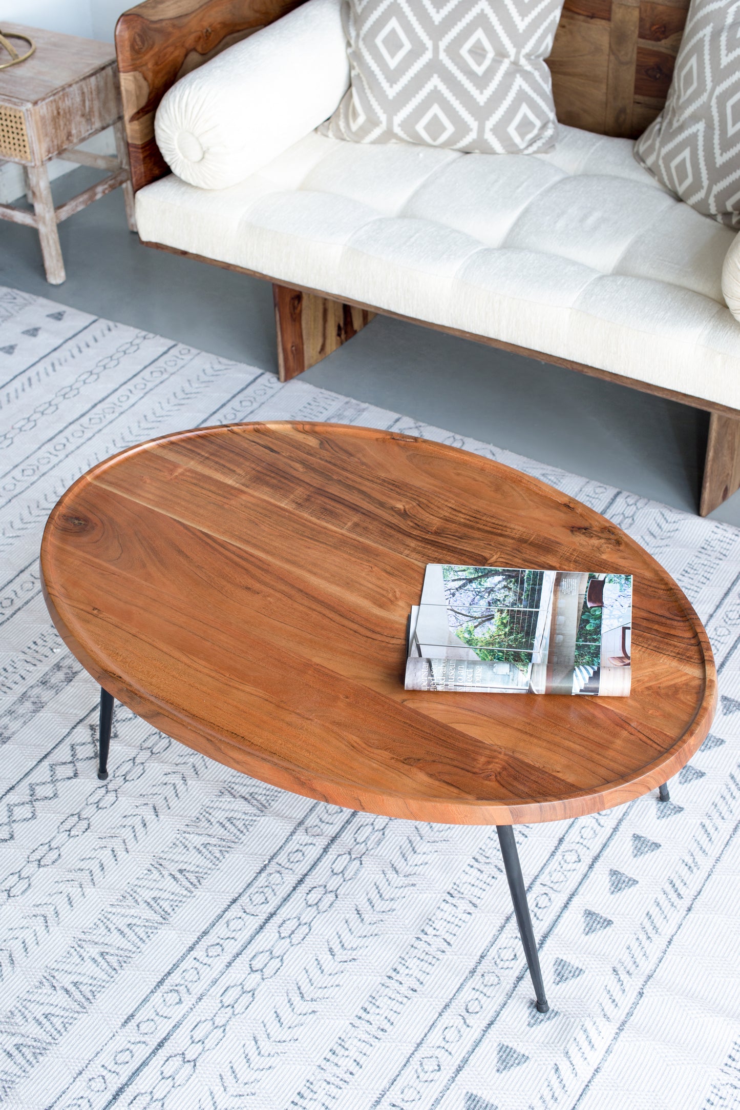Oval natural wood coffee table with thin black legs on a patterned rug