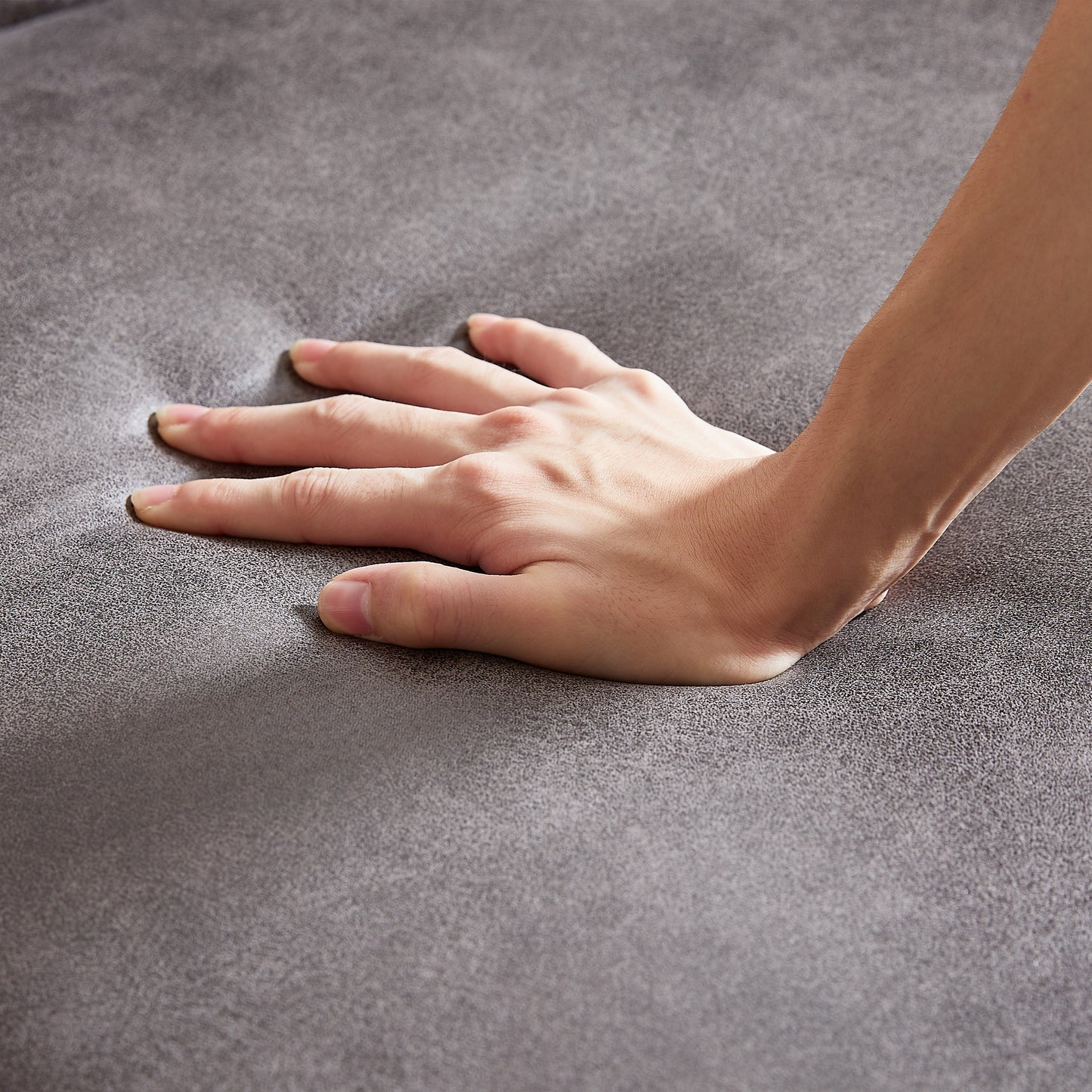 Closeup of a hand pressing into soft grey velvet sofa fabric showing plush comfort