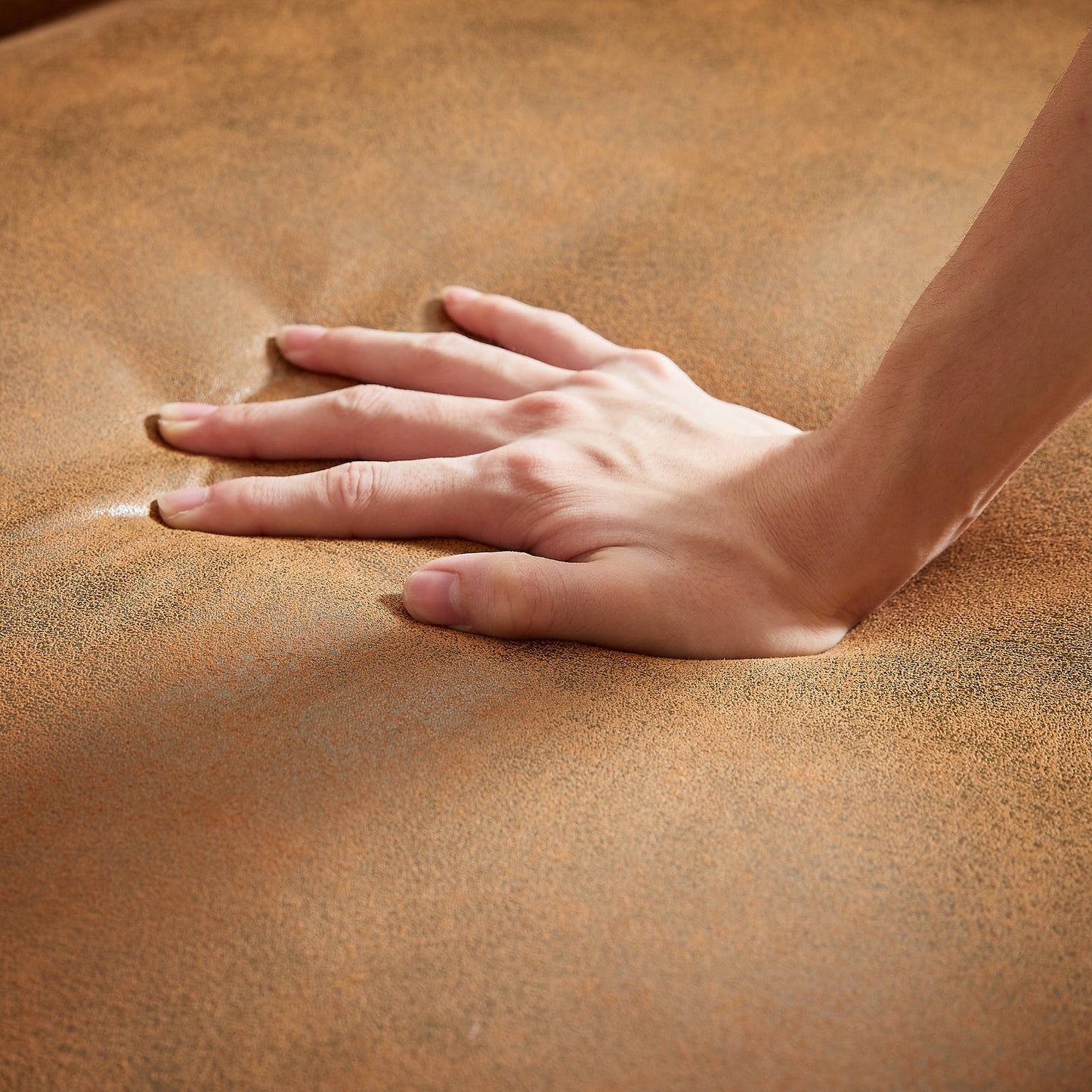 Hand pressing into plush tan microfiber fabric demonstrating comfort and softness