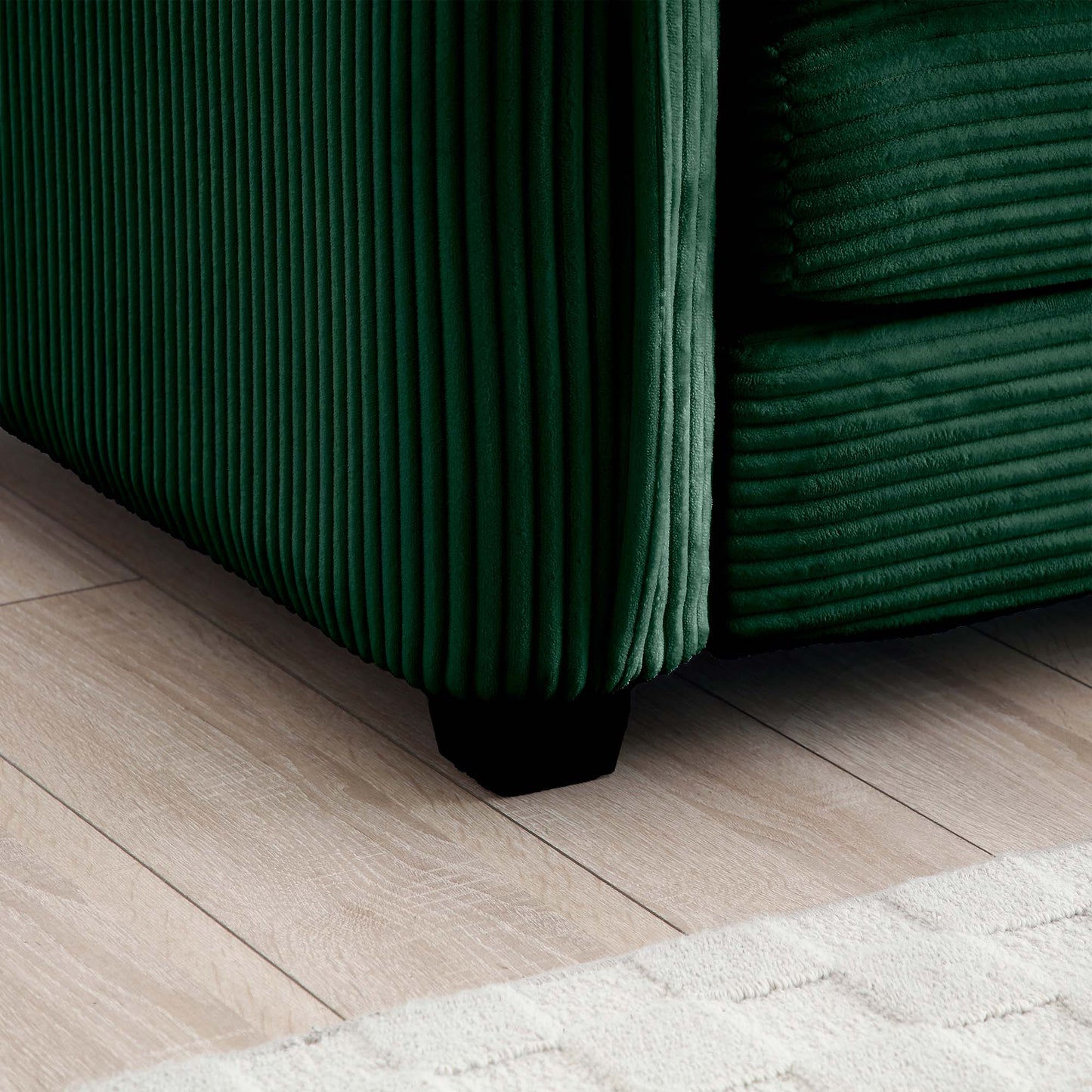 Deep green corduroy sofa detail with ribbed texture and black wooden foot