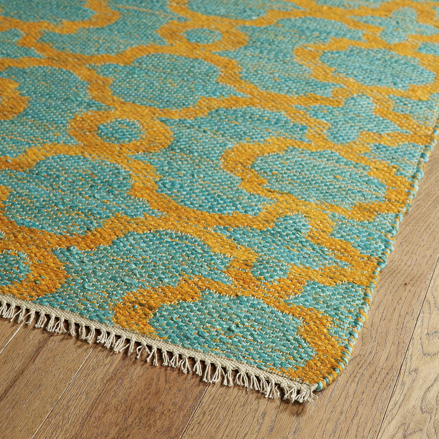Teal and gold geometric woven rug with fringe detail on wood floor