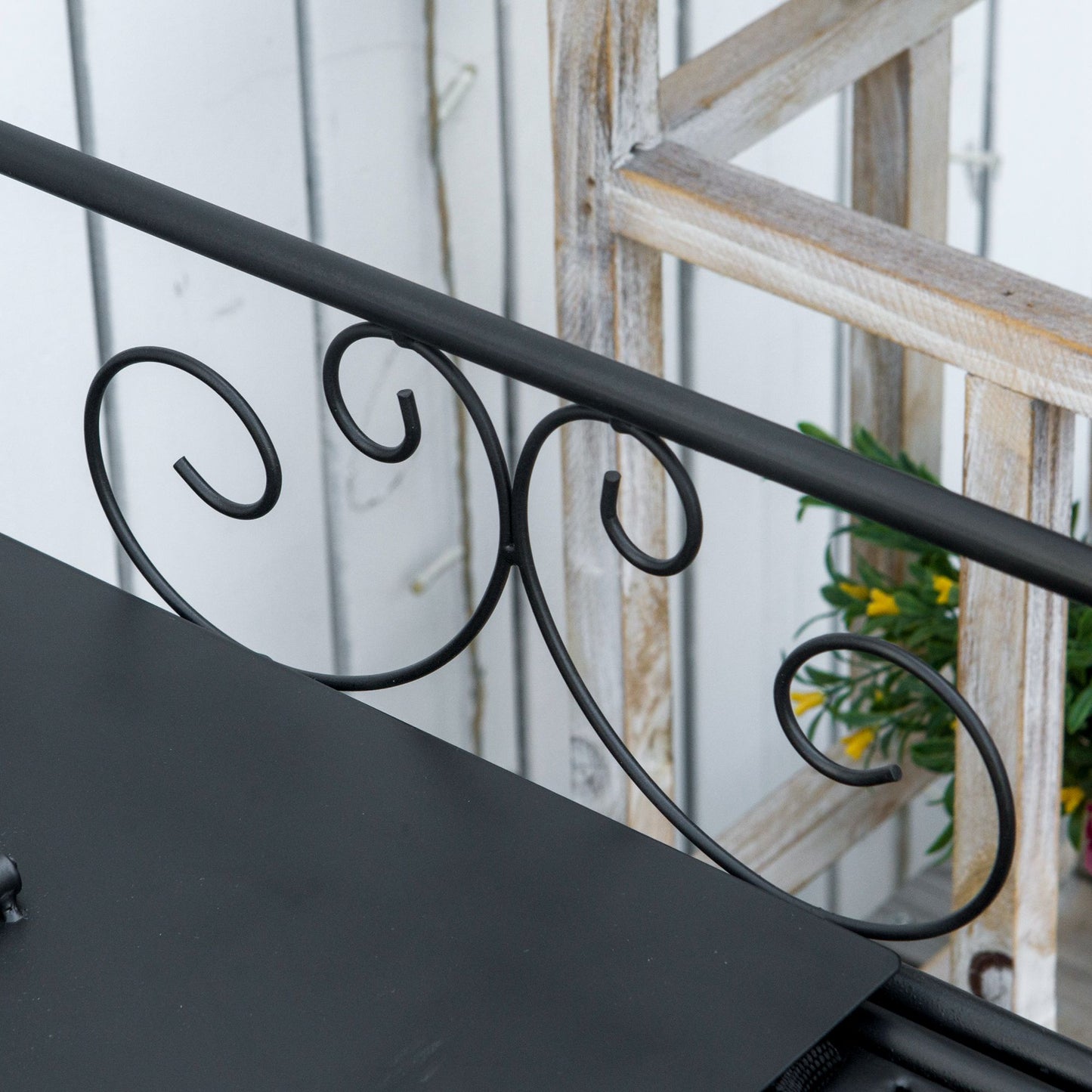 Black metal plant stand with decorative scrollwork and a rustic wooden ladder backdrop