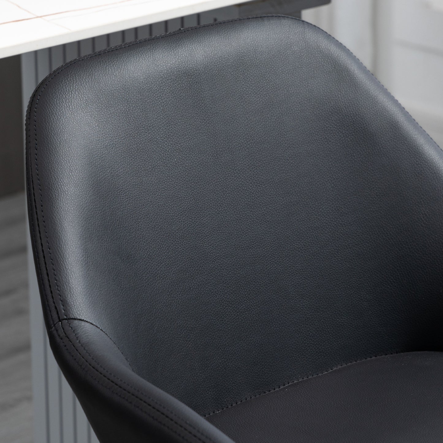 Closeup of a black faux leather dining chair seat and back with detailed stitching