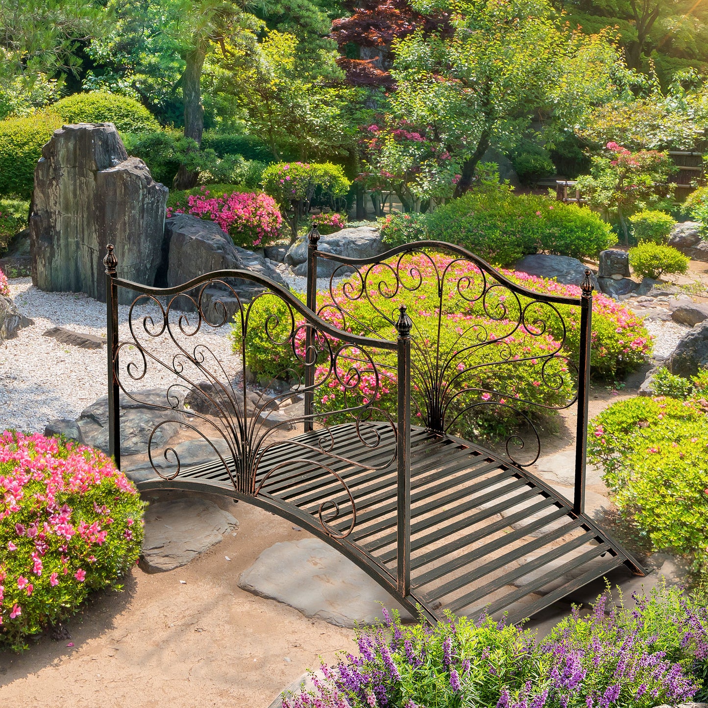 Ornate black metal garden bridge with scrolled detailing set in a lush flowering landscape