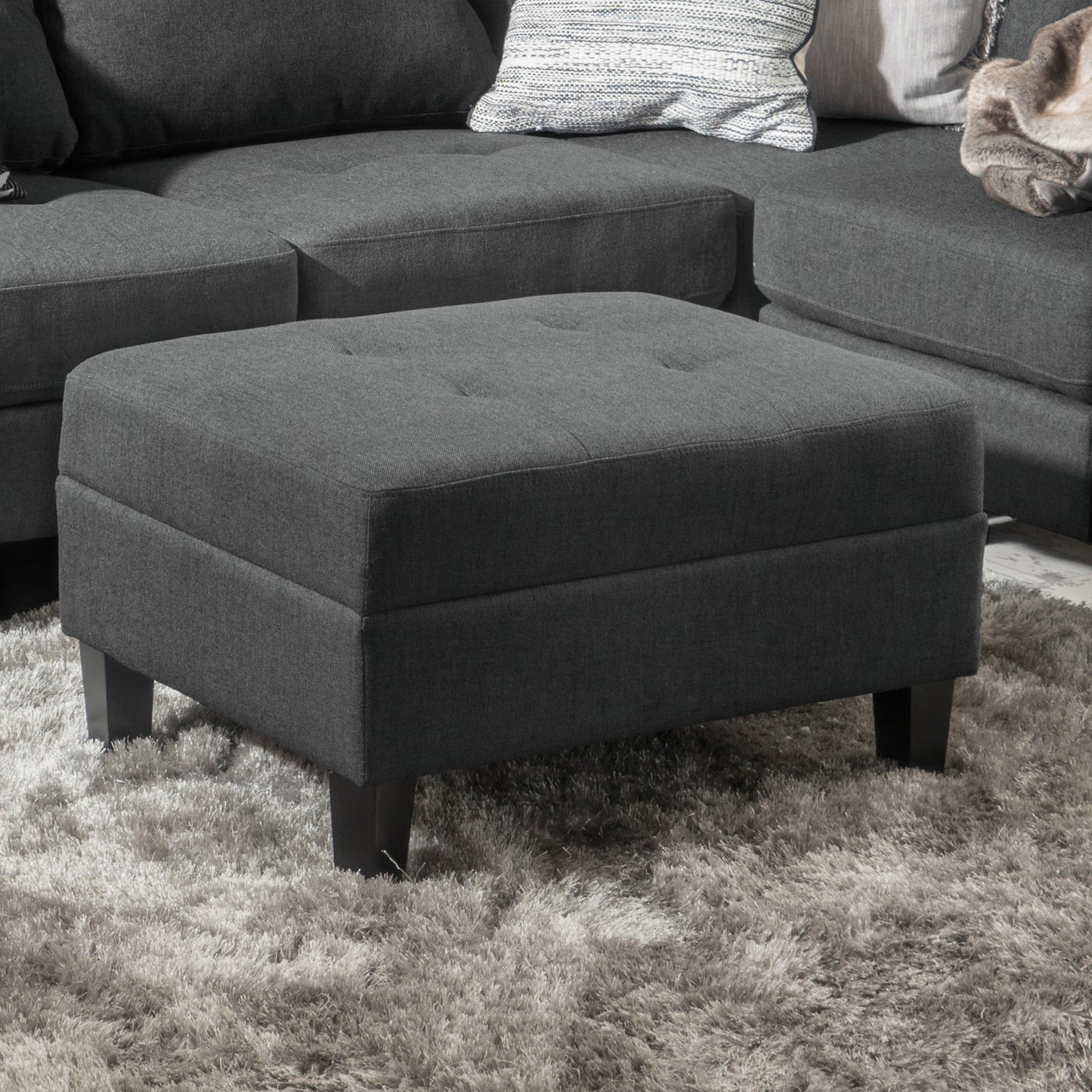 Tufted dark gray fabric ottoman with short wooden legs on a shag rug