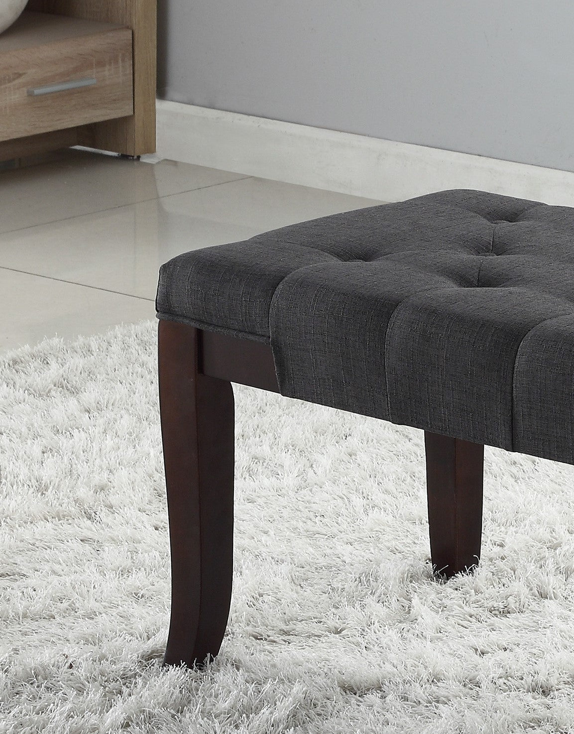 Dark grey tufted upholstered ottoman with dark wood legs on a white rug