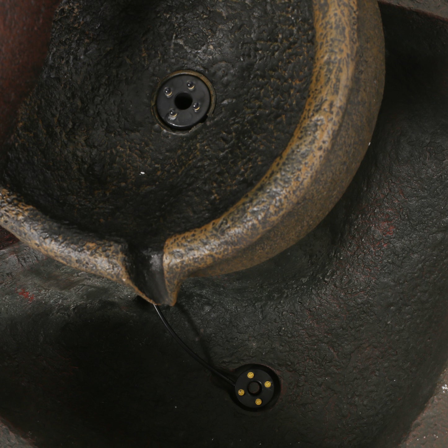 Closeup of a textured dark resin outdoor fountain with a bronze basin and integrated LED lights
