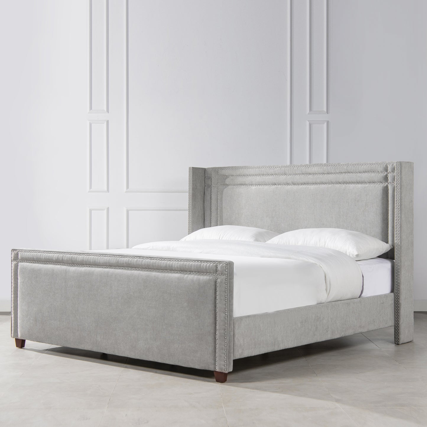 Gray fabric wingback bed with silver nailhead trim and white bedding