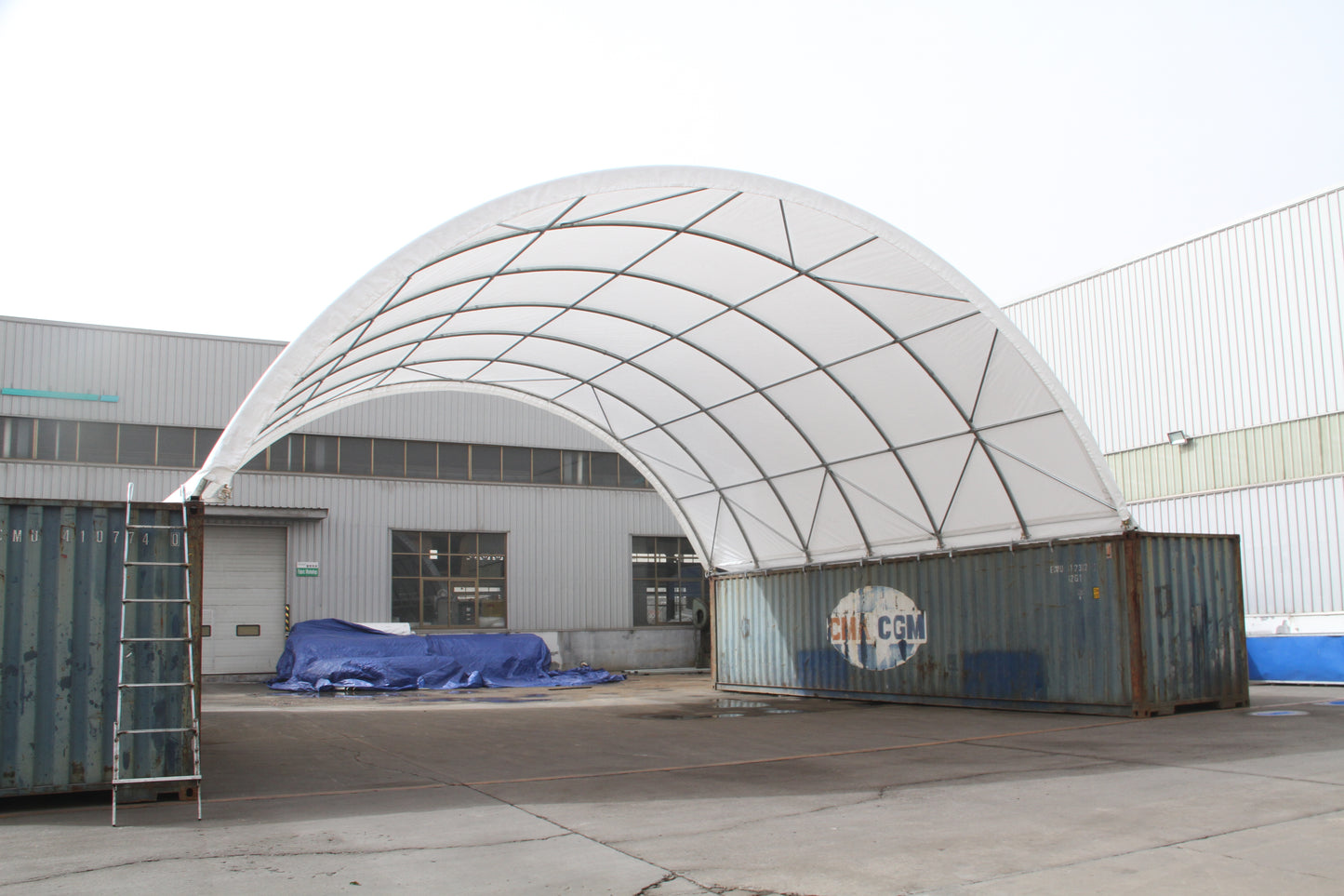 White fabric arch shelter supported by shipping containers ideal for temporary storage