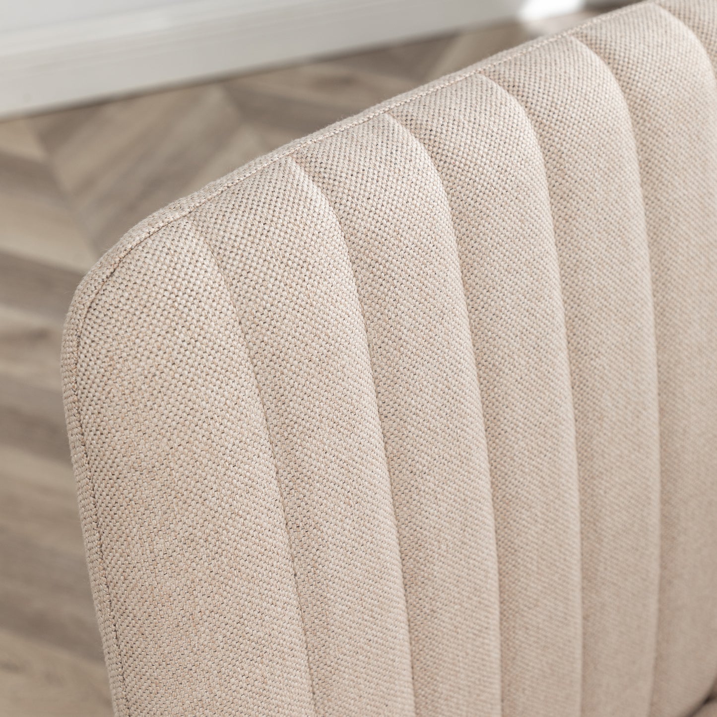 Closeup of beige linen fabric with subtle channel tufting on a dining chair