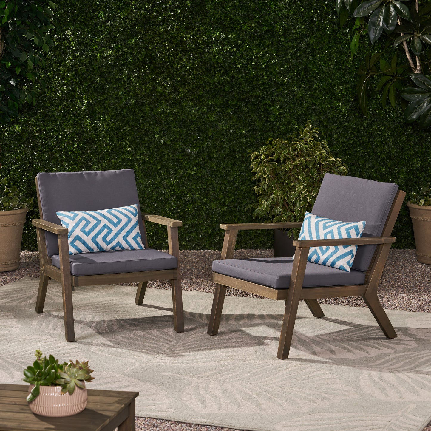 Two modern wooden patio chairs with grey cushions and geometric blue accent pillows
