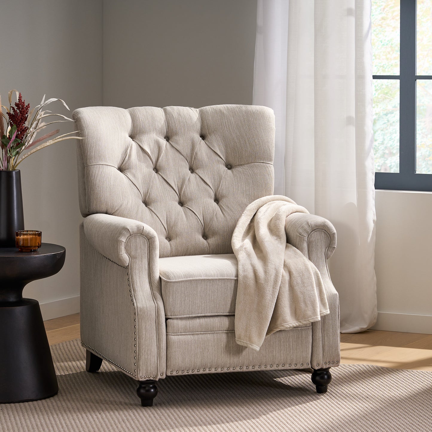 Beige upholstered recliner with tufted back and nailhead trim draped with a cream throw blanket
