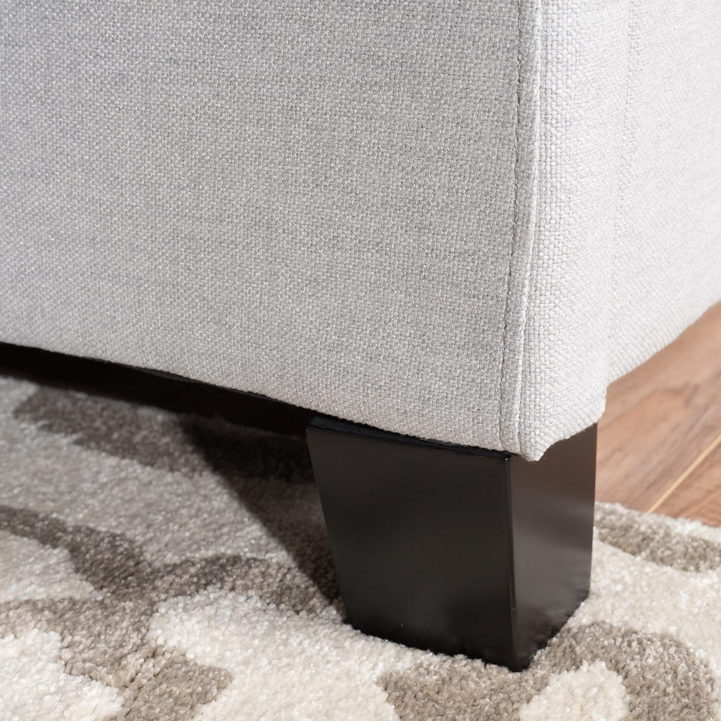 Closeup of textured light grey fabric on a sofa arm with a dark wood leg on a geometric rug