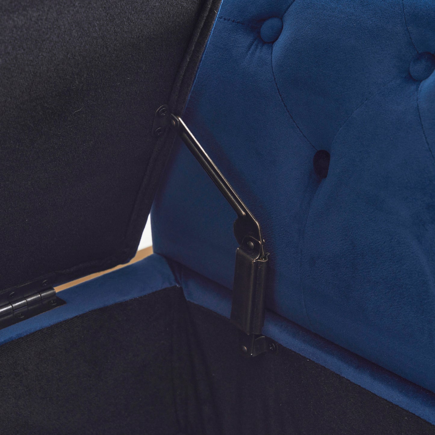 Closeup of a dark blue velvet storage ottoman with a metal hinge mechanism visible