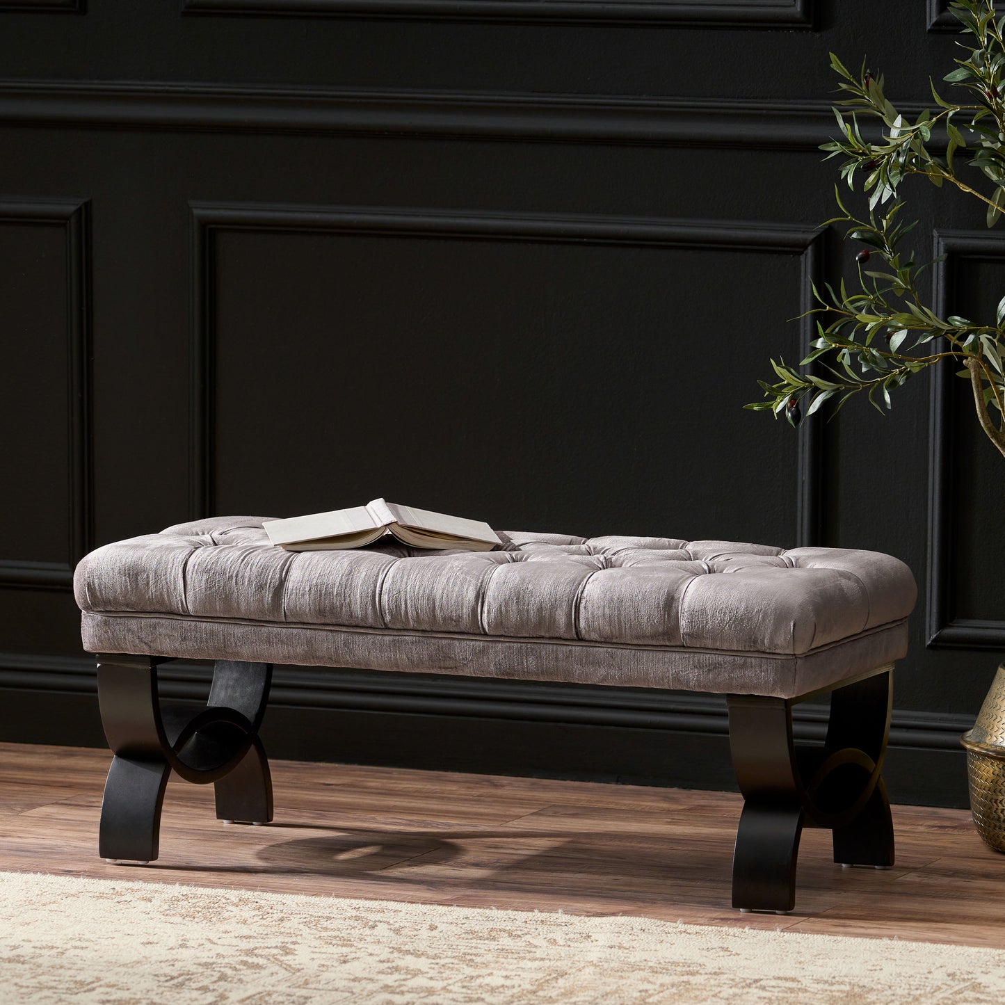 Tufted grey velvet bench with a book on top and black curved legs