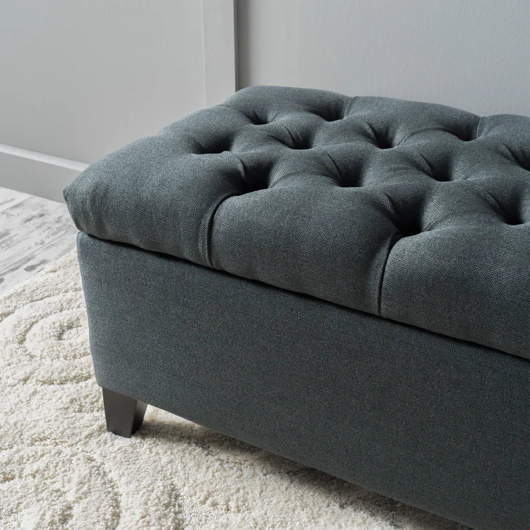 Dark grey tufted storage ottoman with wooden legs on cream rug