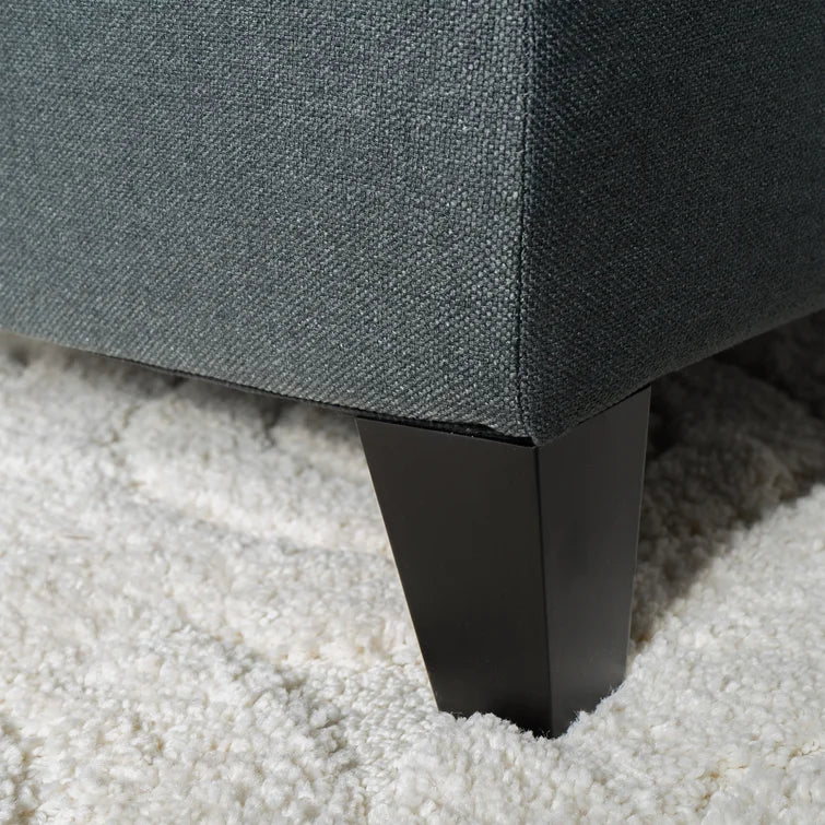 Closeup of dark gray textured fabric sofa arm with square dark wood legs on a white shag rug