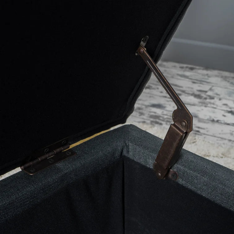 Dark grey upholstered storage ottoman with bronze hinge open lid showing black lining