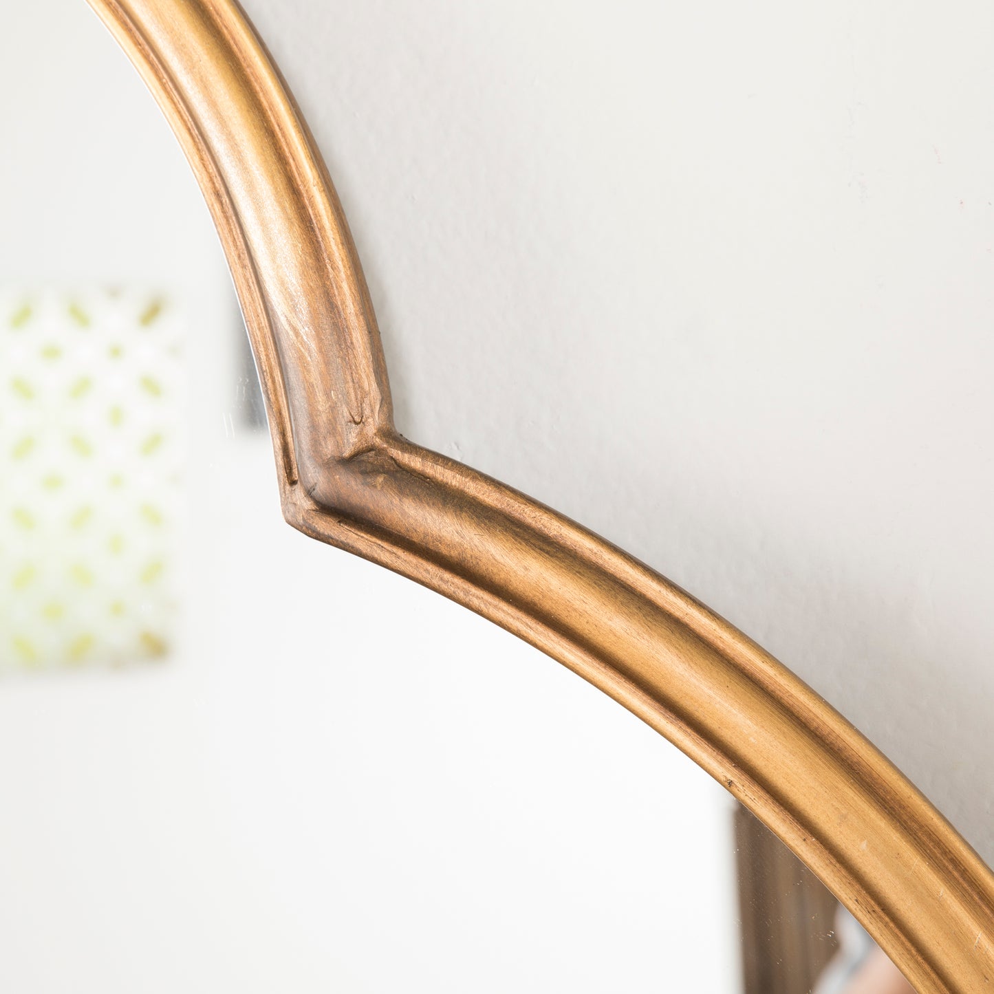 Antique gold ornate mirror frame with subtle wood grain texture reflecting a blurred patterned background