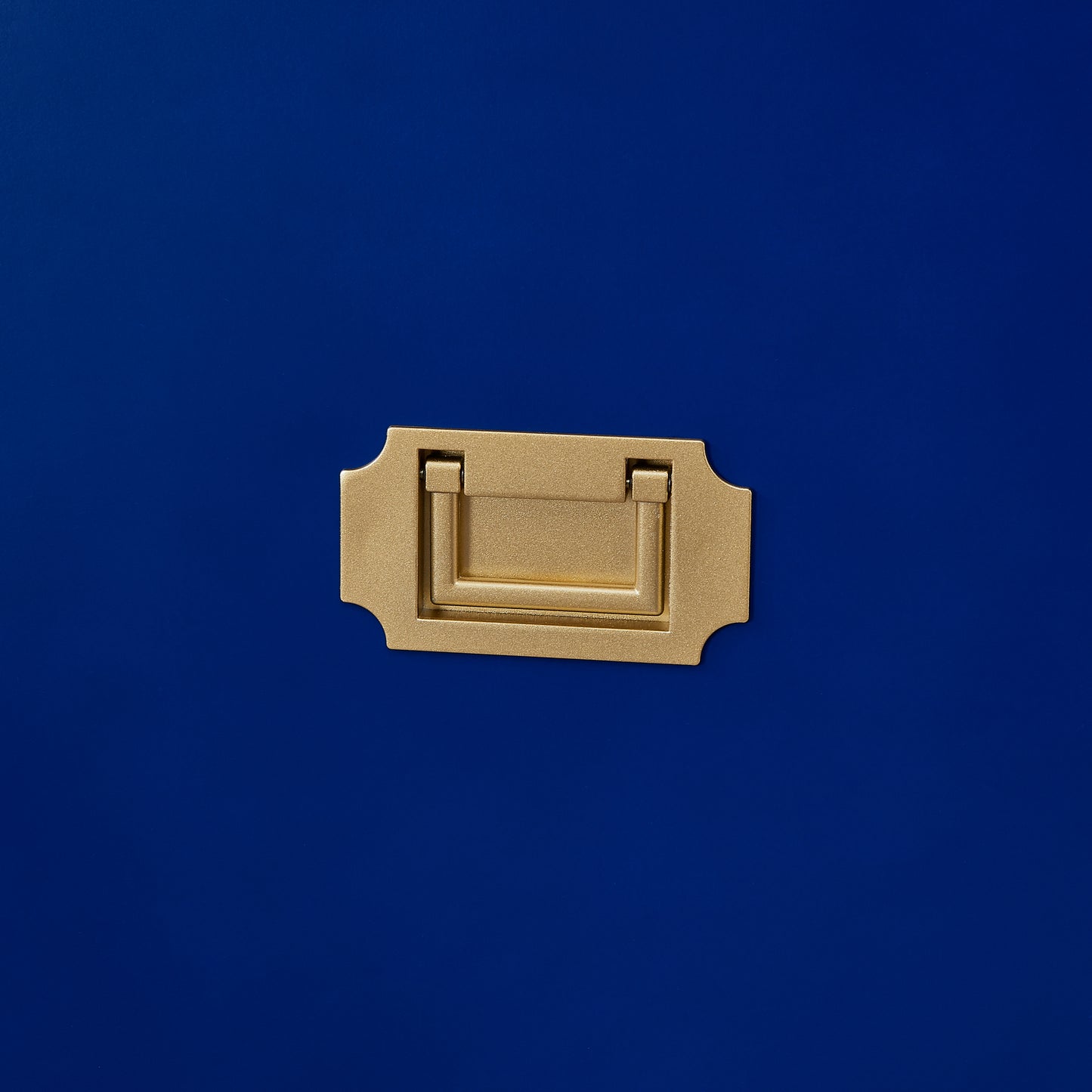 Brushed brass campaign handle with decorative backplate on navy blue surface