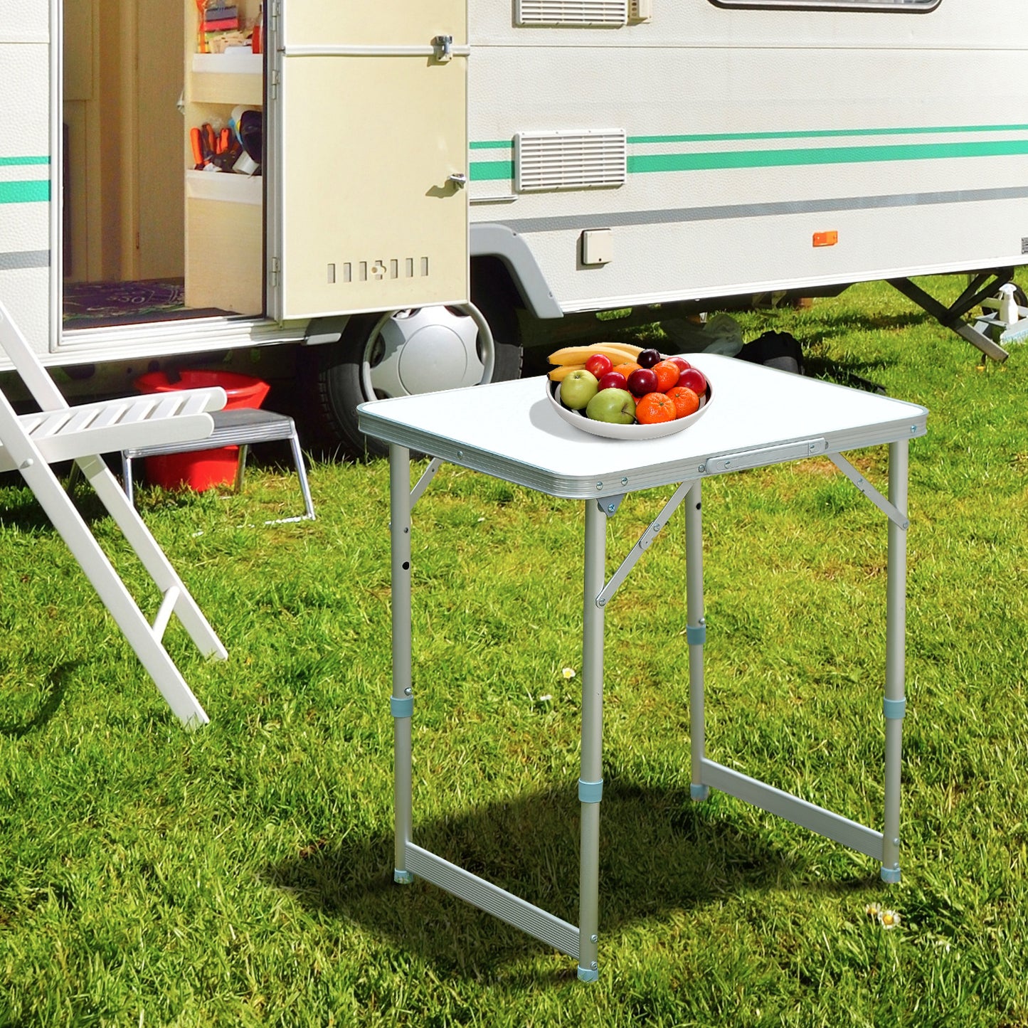 Portable folding table with adjustable height legs set up on grass next to an RV