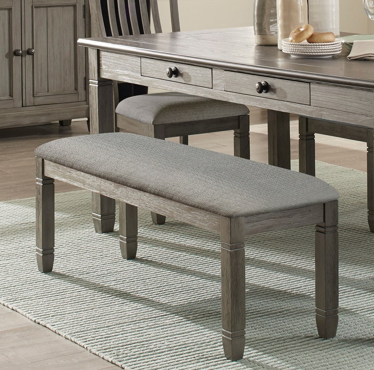 Gray upholstered dining bench with distressed wood legs and matching dining table