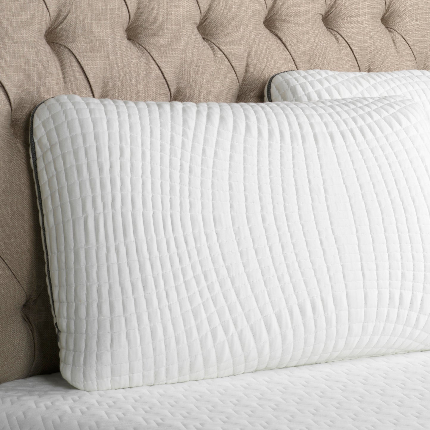 Quilted white bolster pillow with subtle textured fabric detail on a tufted headboard
