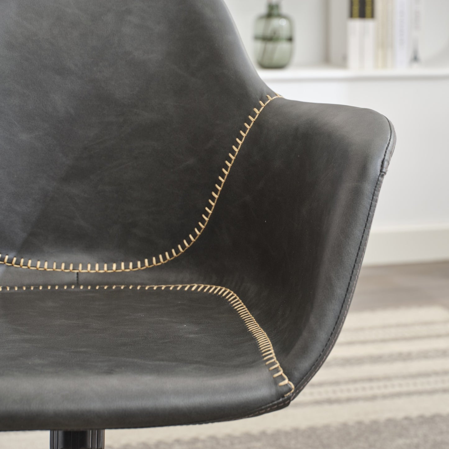 Closeup of a dark grey faux leather chair with contrasting tan stitching offering a modern accent