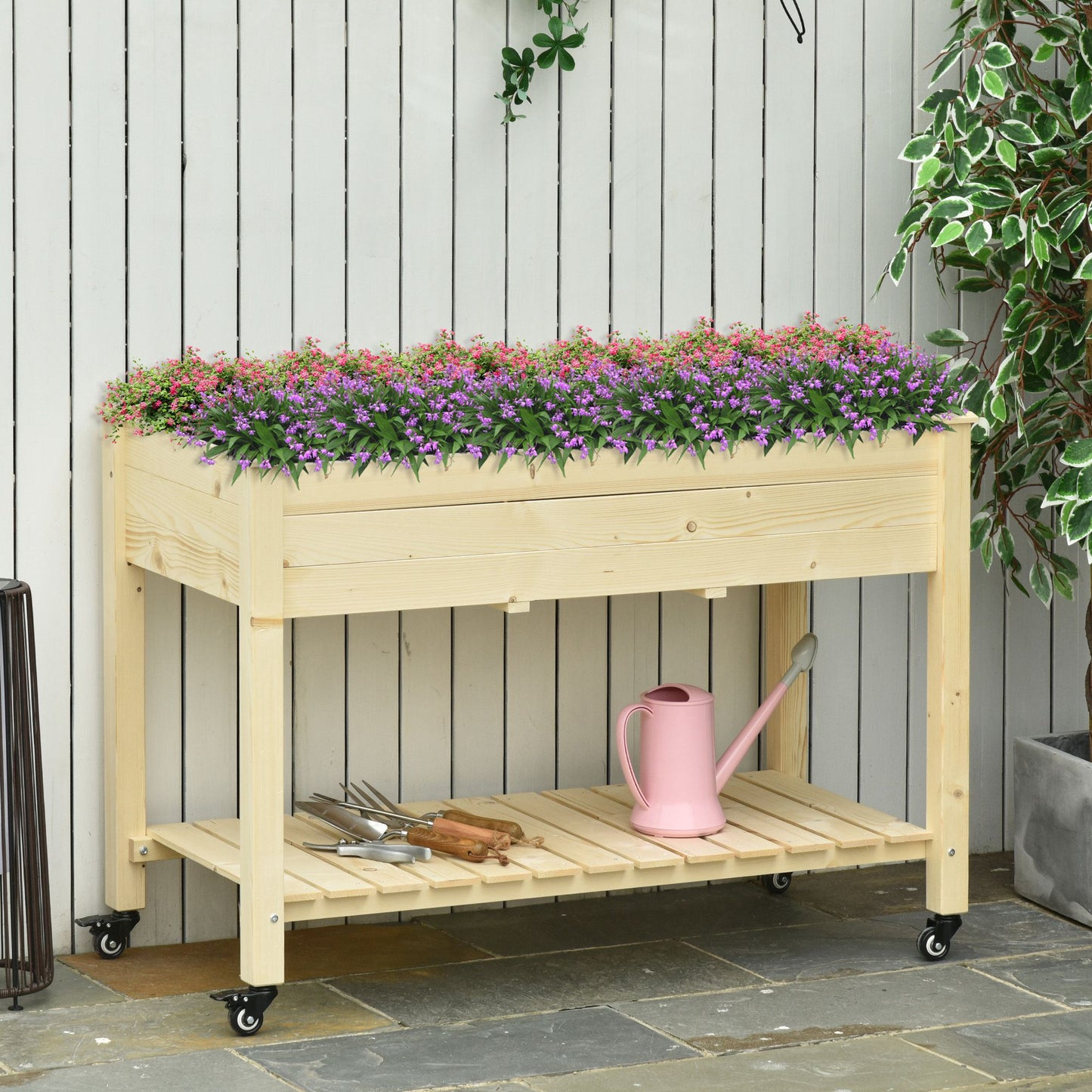 Wooden raised garden bed with pink and purple flowers and gardening tools