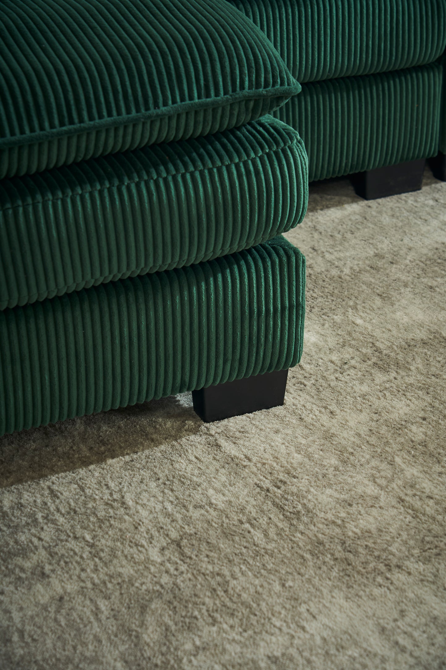 Plush emerald green corduroy sofa cushions stacked for comfort featuring a soft ribbed texture and modern black legs