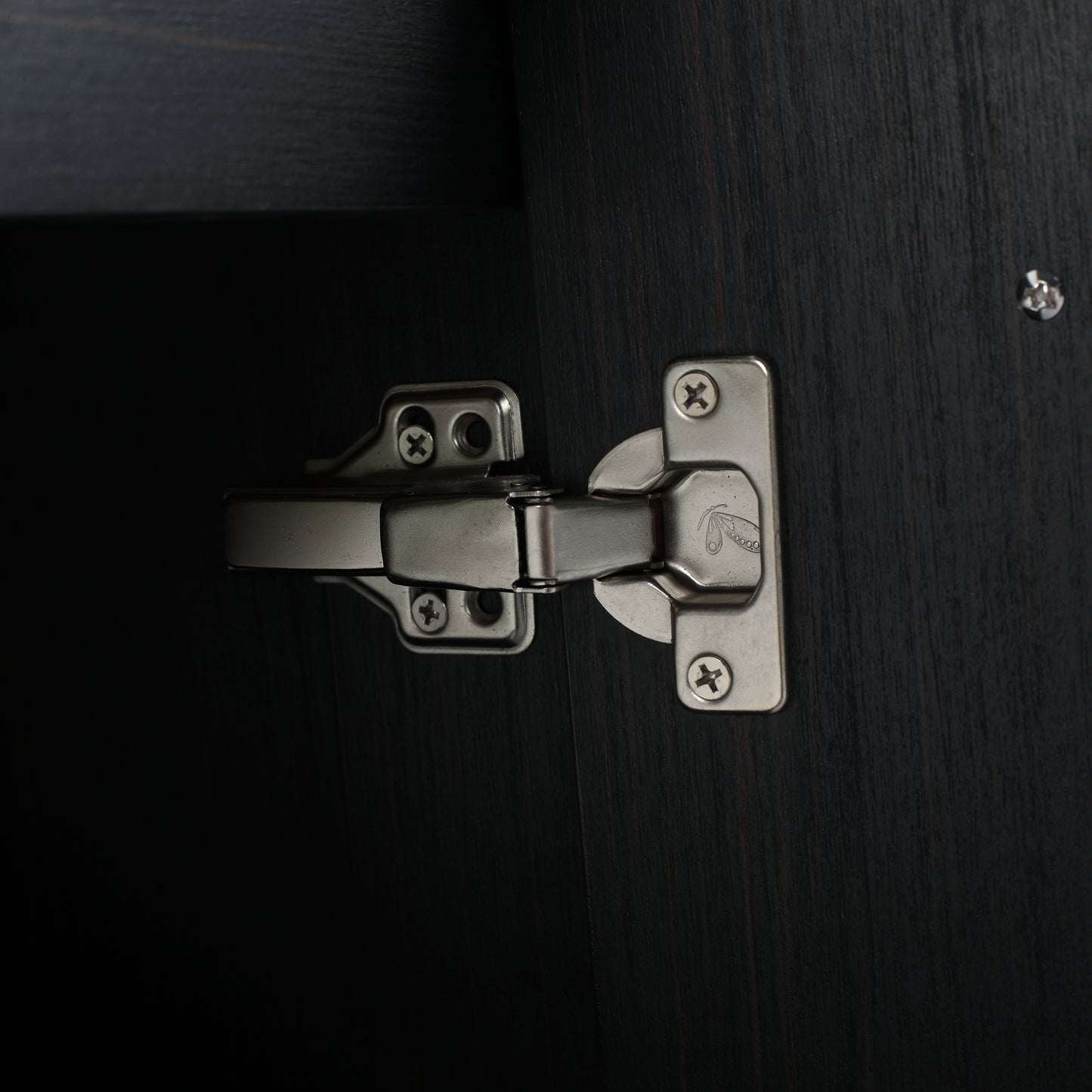 Closeup of a brushed nickel cabinet hinge on dark wood grain