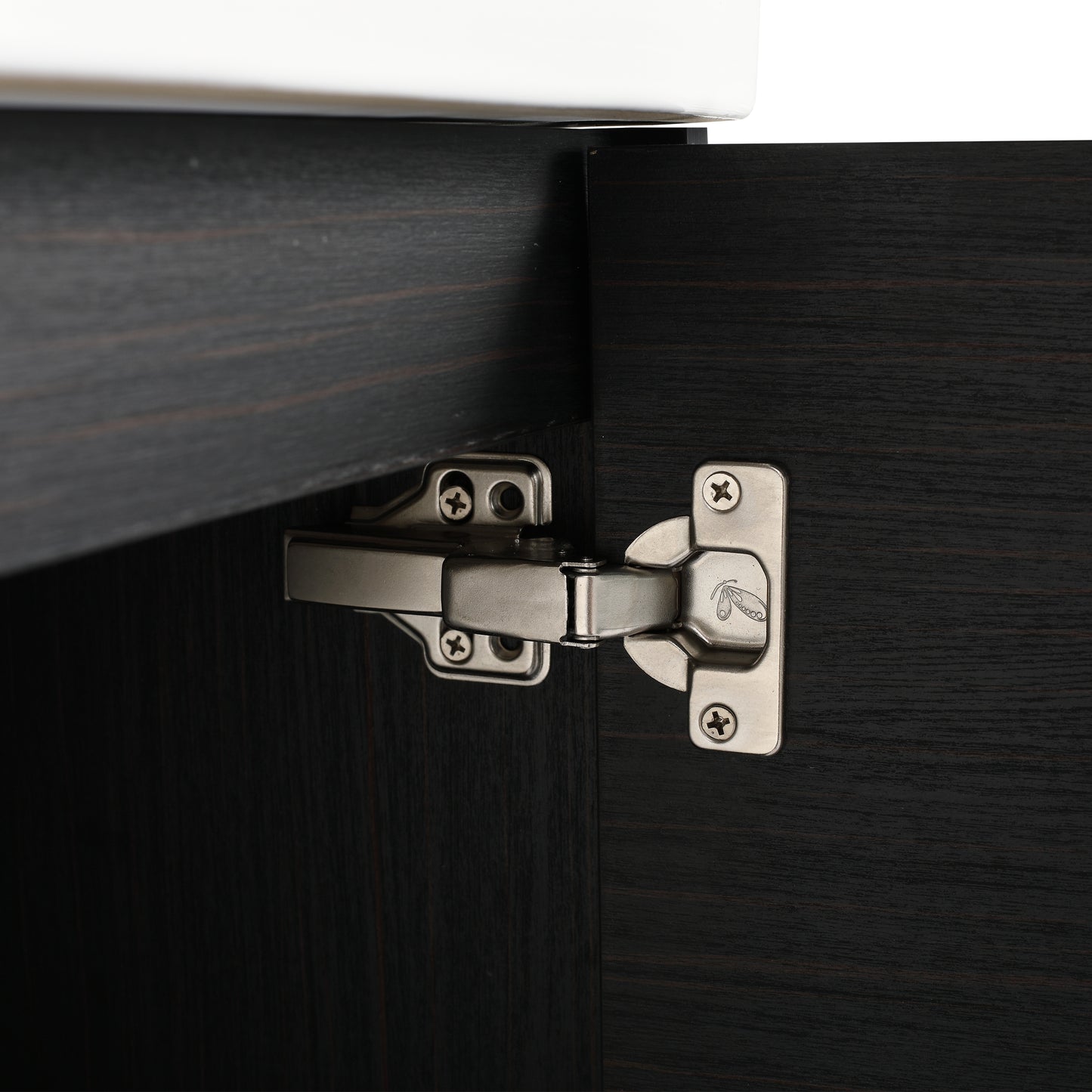 Closeup of a brushed nickel cabinet hinge attached to dark wood grain cabinetry