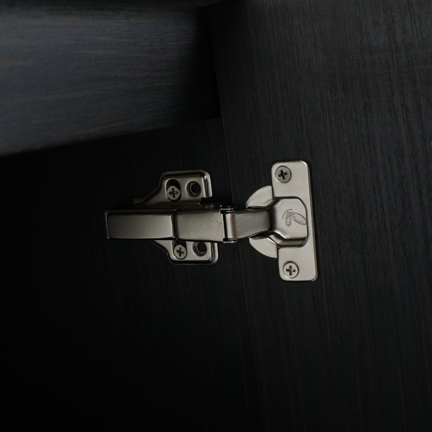 Closeup of a brushed nickel cabinet hinge attached to dark wood for furniture assembly