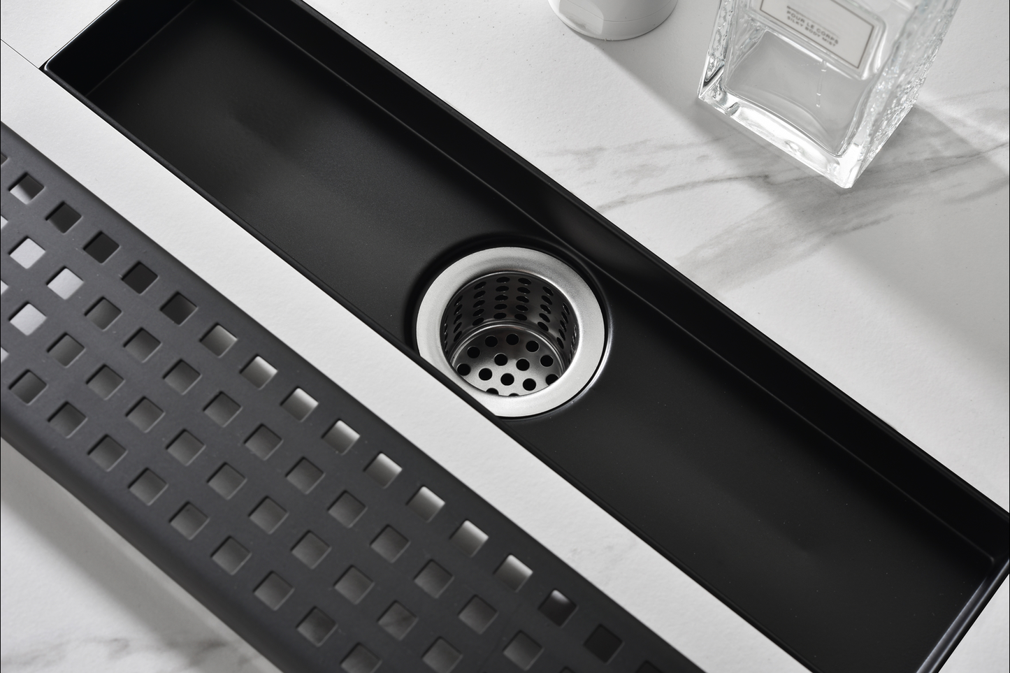 Sleek black linear drain with a perforated stainless steel strainer for a modern bathroom