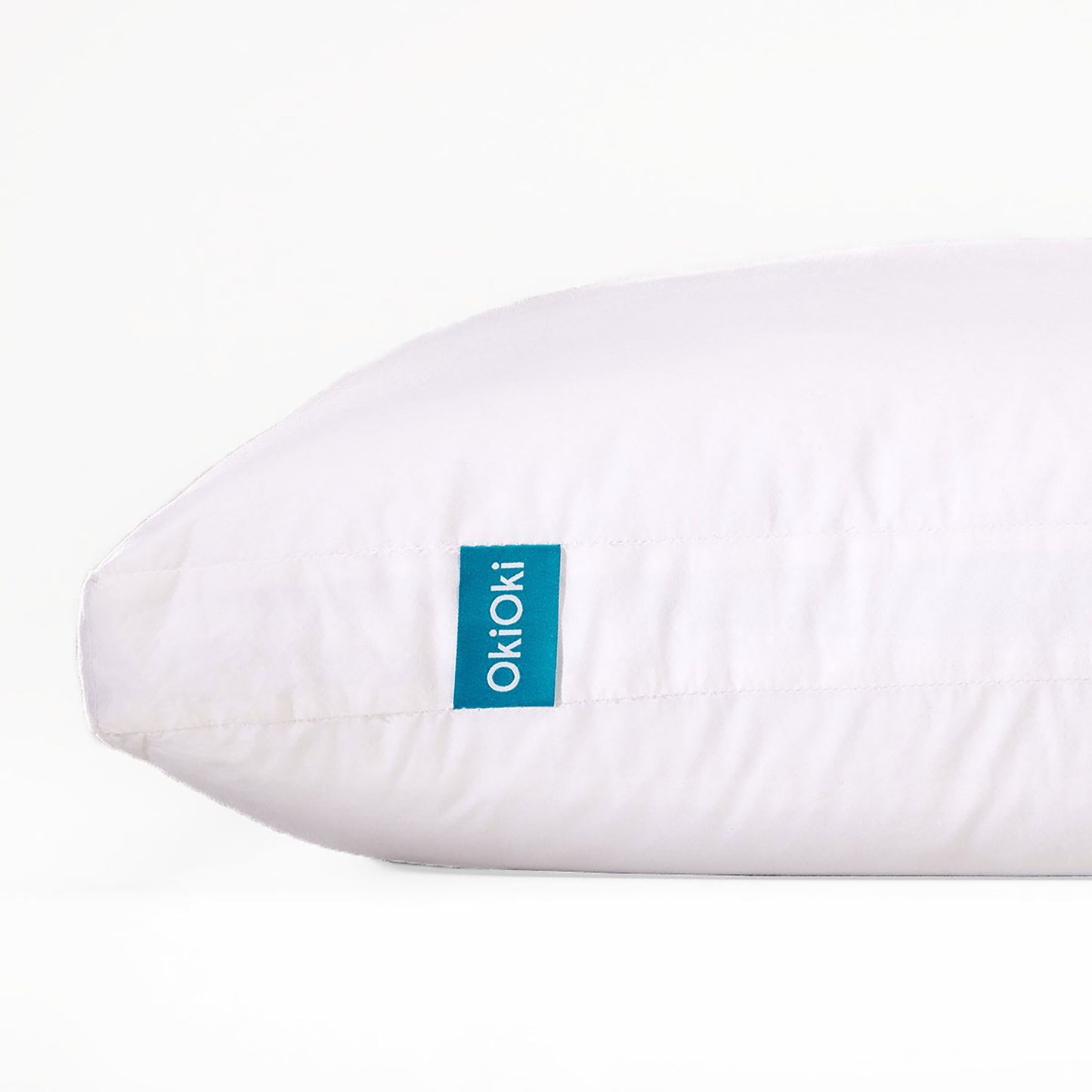 A soft white OkiOki pillow with a turquoise tag offering comfortable support for your head