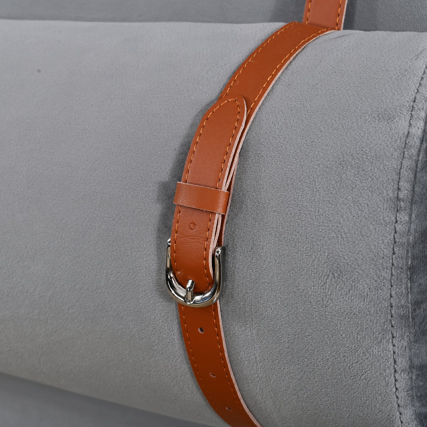 Closeup of a grey plush fabric roll secured by a brown leather strap with a silver buckle