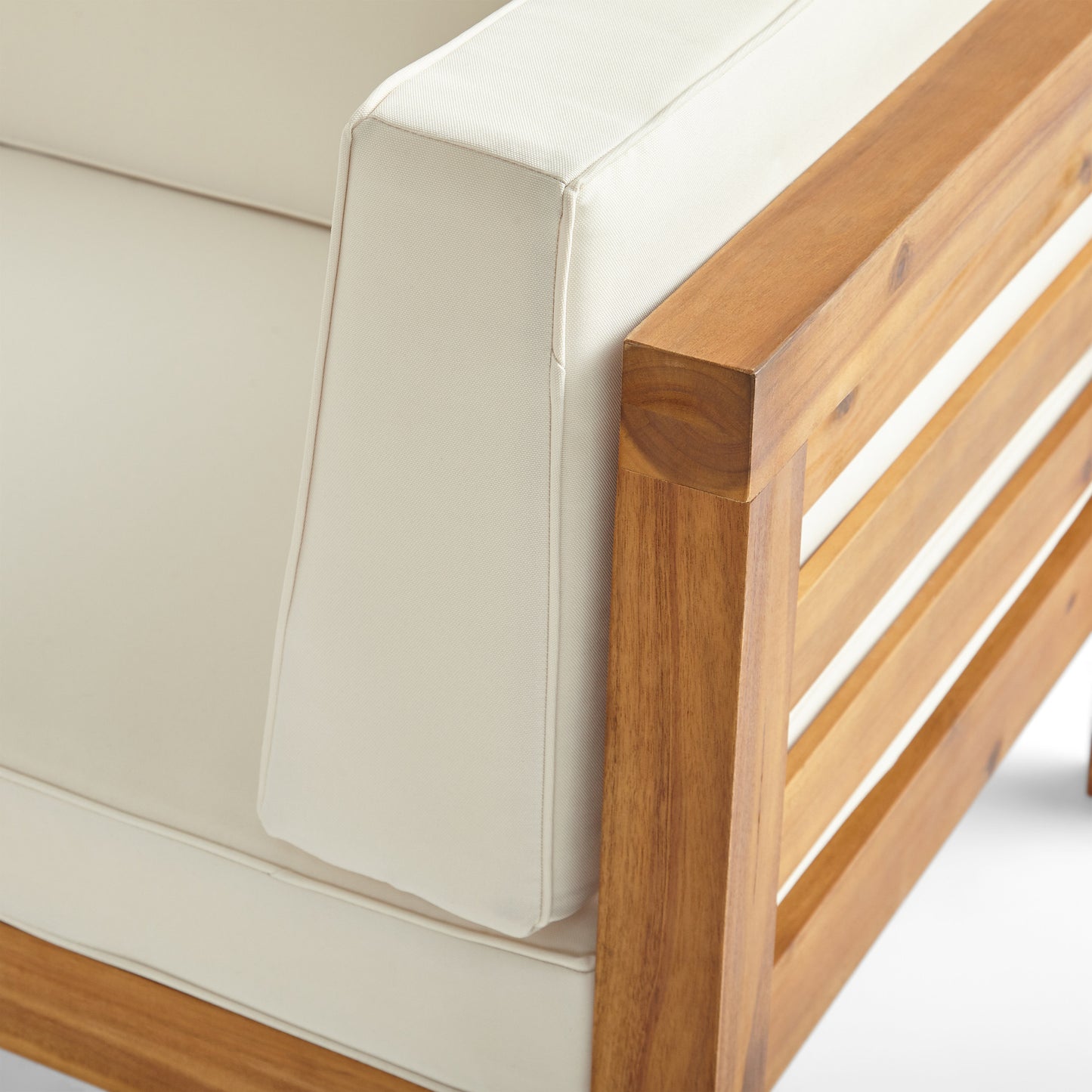Closeup of a modern teak wood outdoor armchair with cream cushions