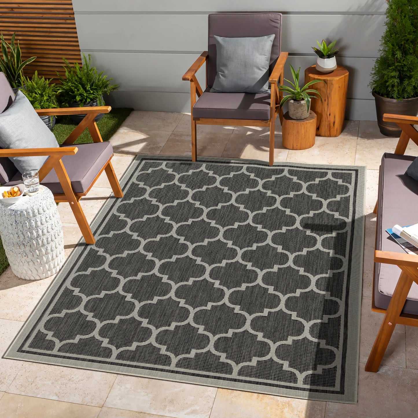 Dark grey outdoor rug with white quatrefoil pattern and striped border