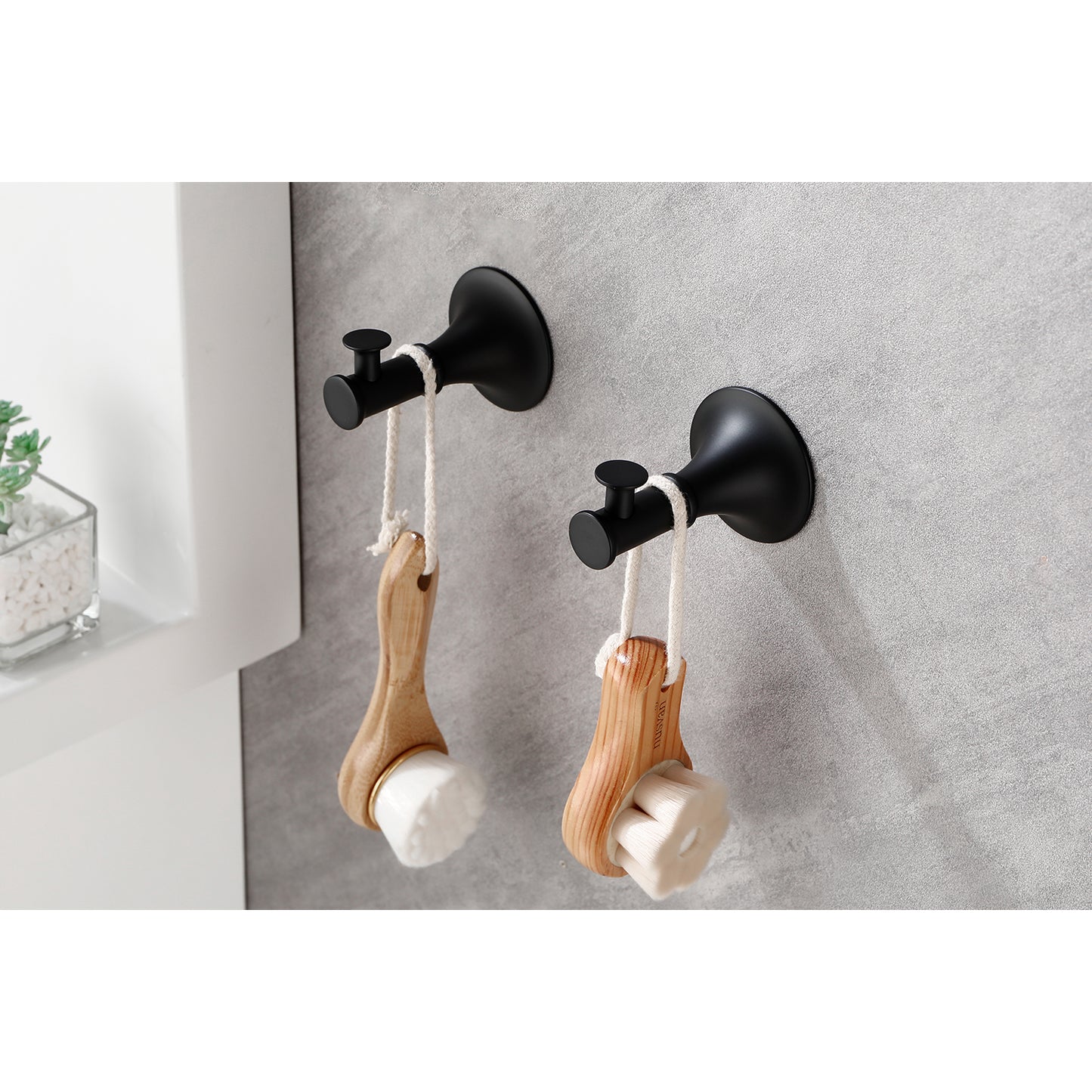 Two black bathroom hooks holding wooden face cleansing brushes with white bristles