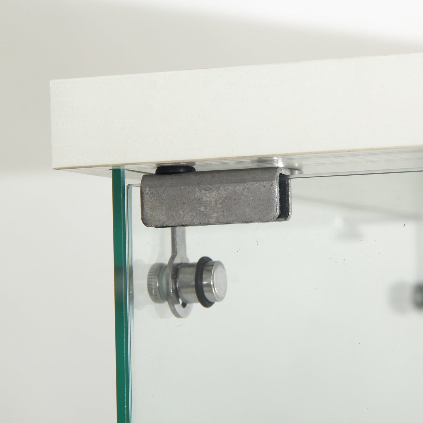 Metal cabinet hinge with screws securing a glass shelf to a white top panel