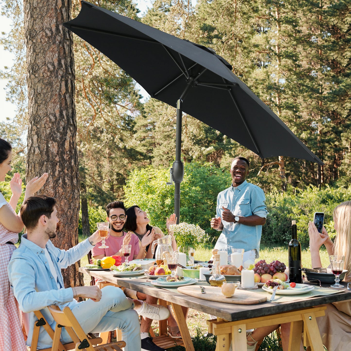 Black patio umbrella provides shade for an outdoor picnic with friends enjoying food and drinks